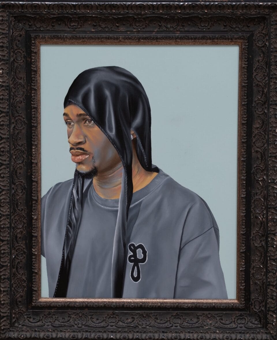 a framed portrait of a Black man in a gray sweatshirt, wearing an untied black durag on his head, set against a light blue background