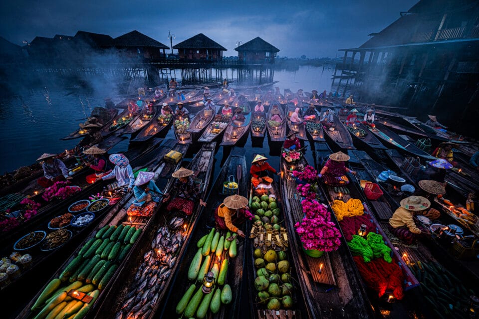 an overview of a floating market on a lake in Myanmar, with long boats full of fruits and other foods