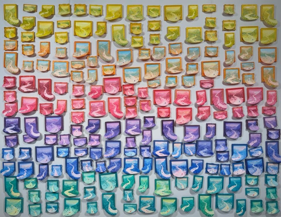 dozens of miniature paintings depicting winter landscapes spilling out of ornate frames, affixed to a white wall in a colorful gradient from yellow, to pink, to purple, and teal