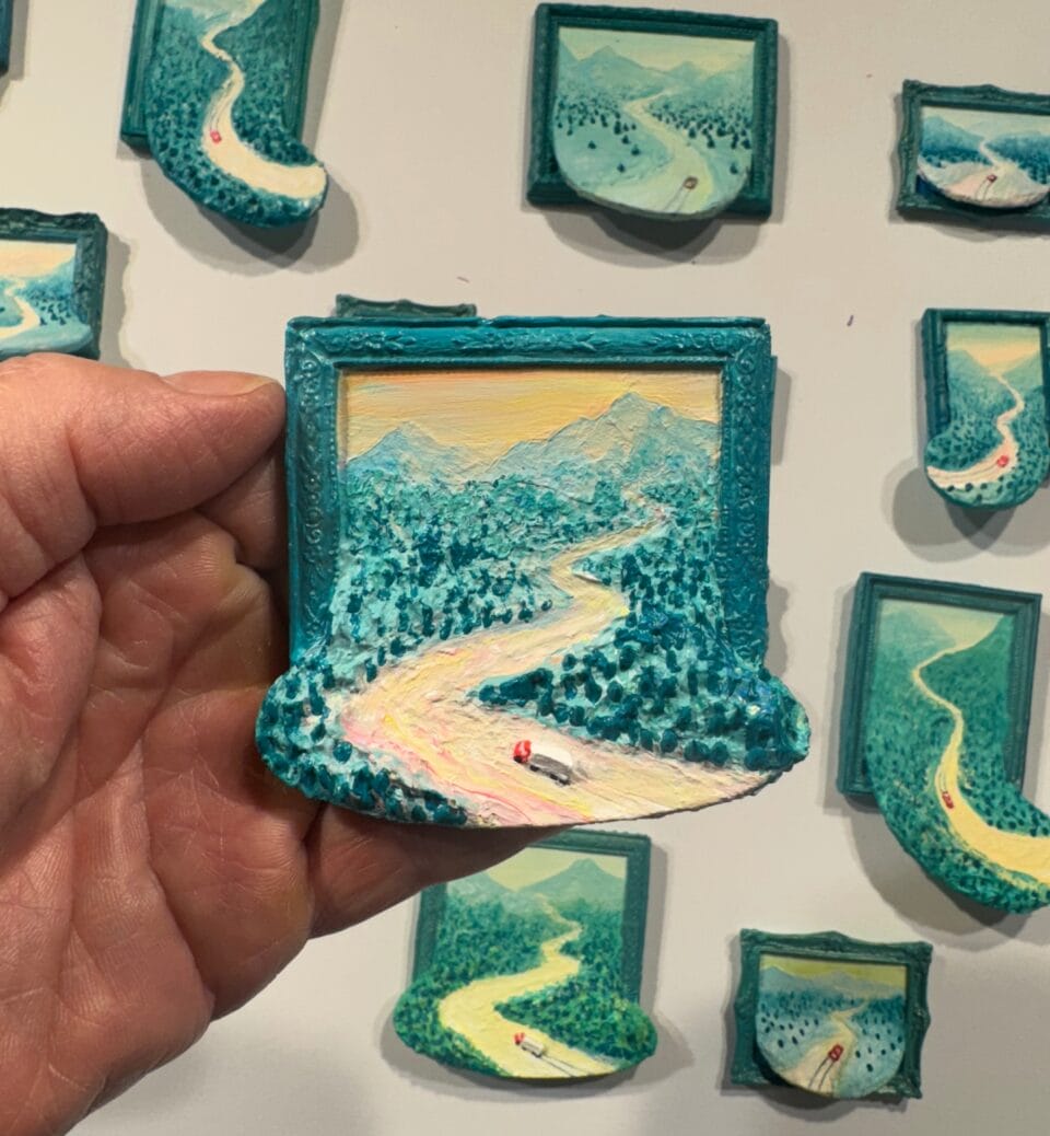 a miniature painting depicting a teal landscape spilling out of the ornate frame. more paintings of the same dominating color are affixed to a white wall in the background