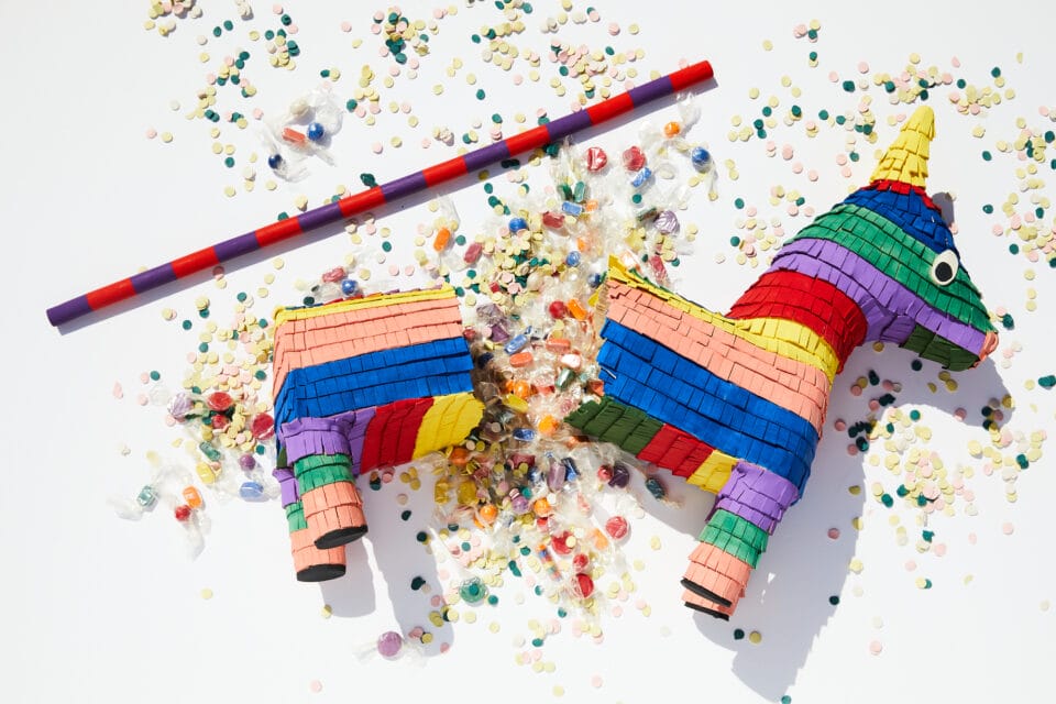 a ceramic sculpture of a broken piñata and striped stick. candy and confetti cover the ground underneath