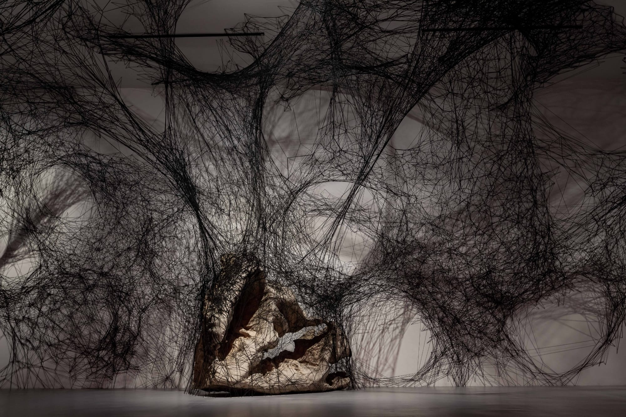black string spreads across a gallery and wraps large rocks