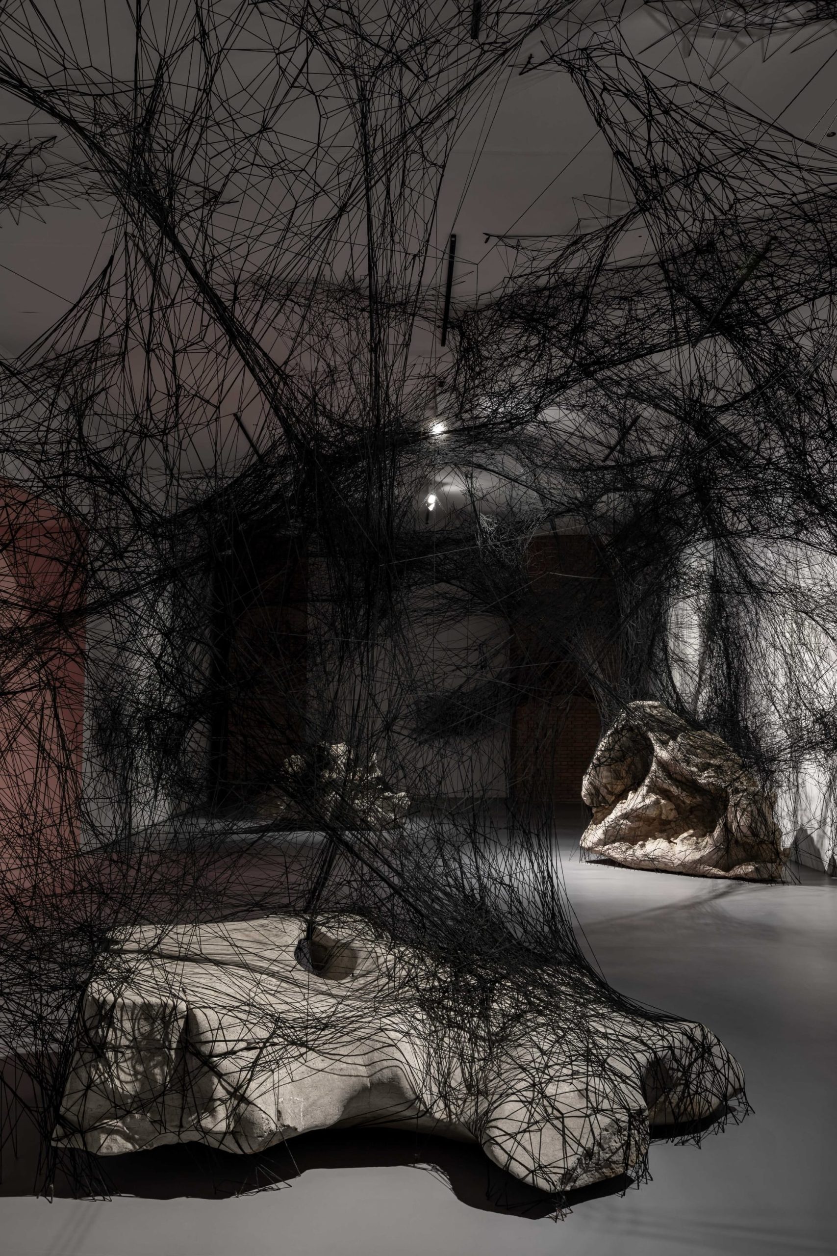 black string spreads across a gallery and wraps large rocks
