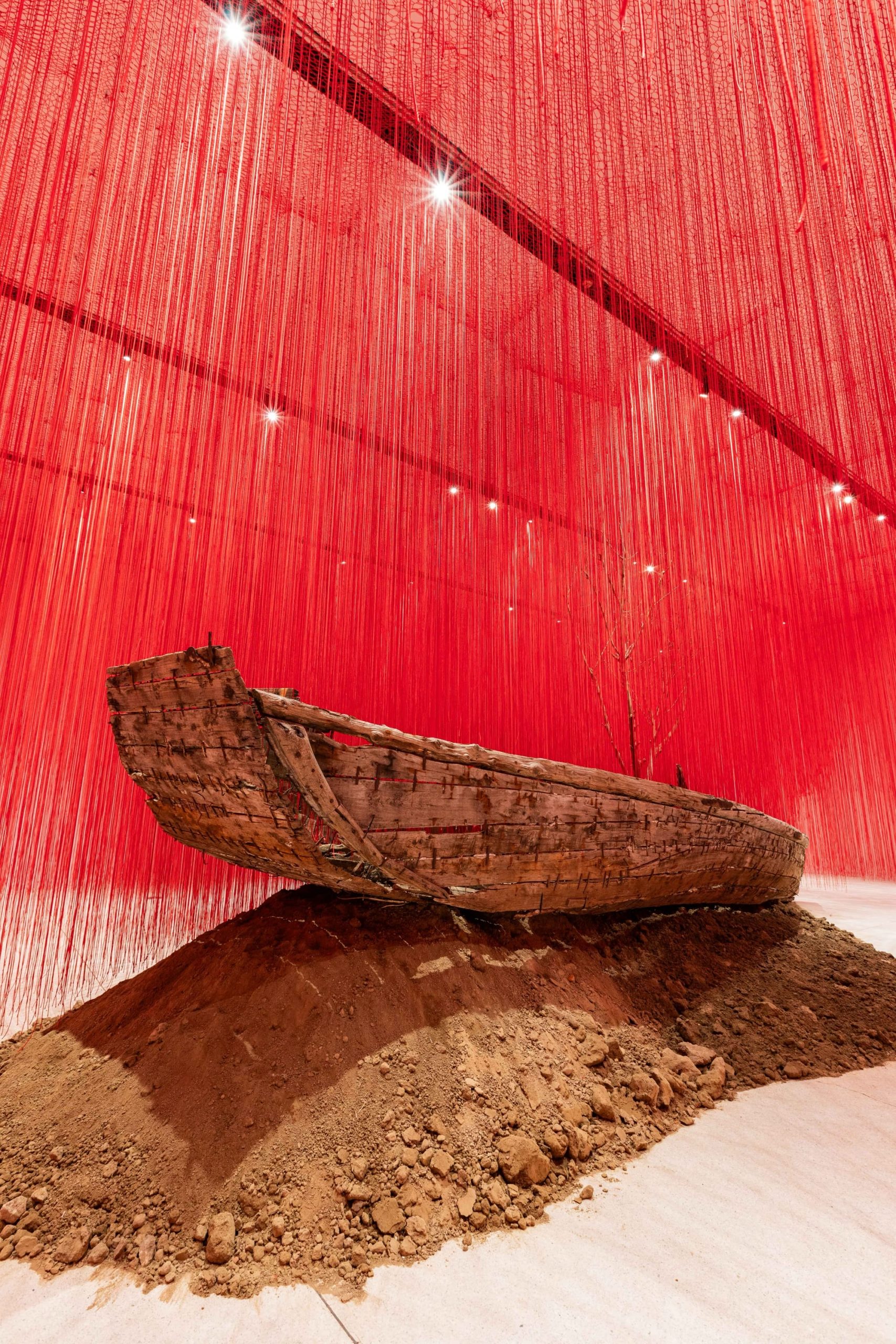 red string drapes around a wooden boat atop a pile of soil