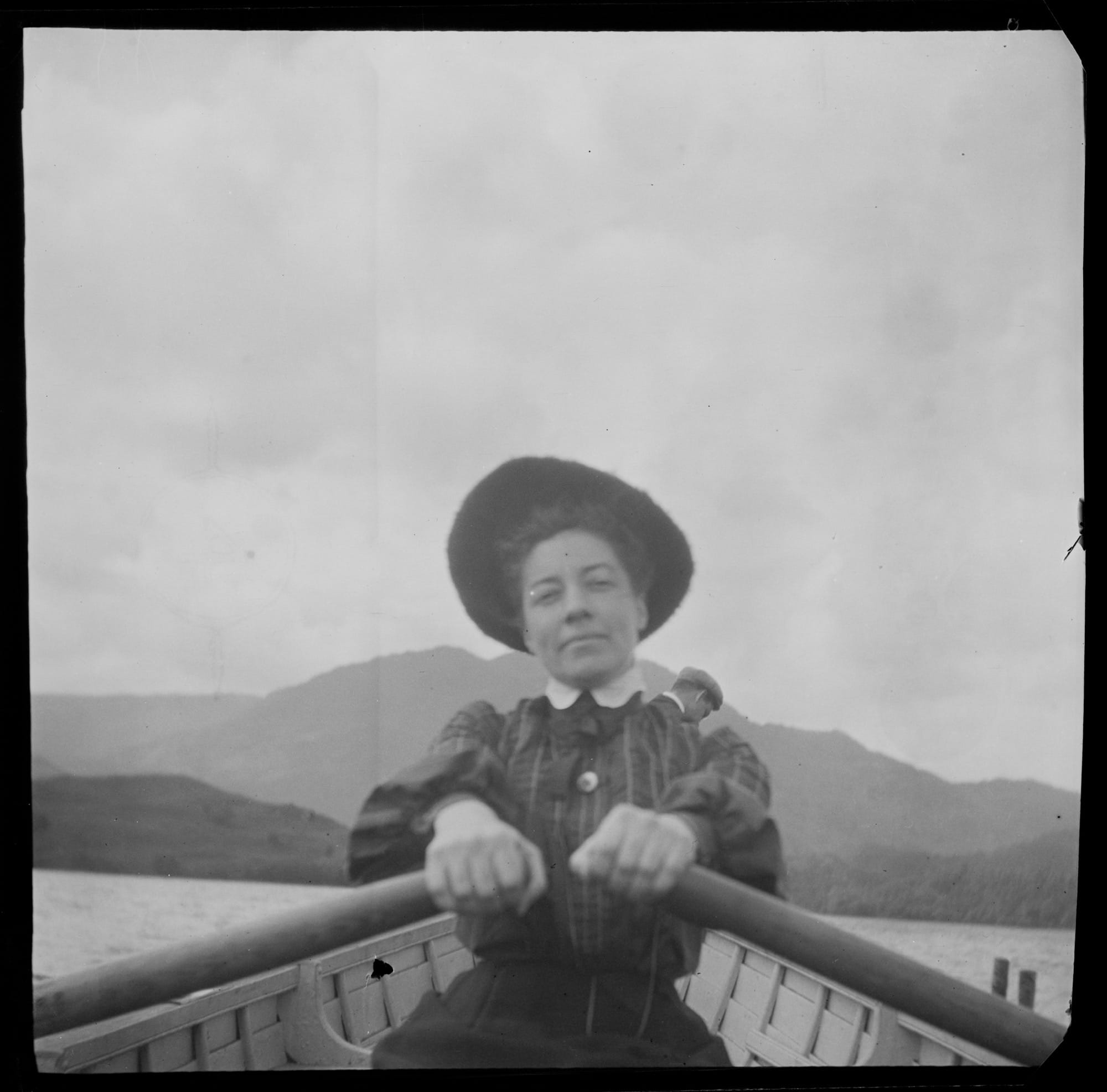 a black-and-white photo from the late 19th century of photography Alice Austen rowing a boat through a hilly landscape