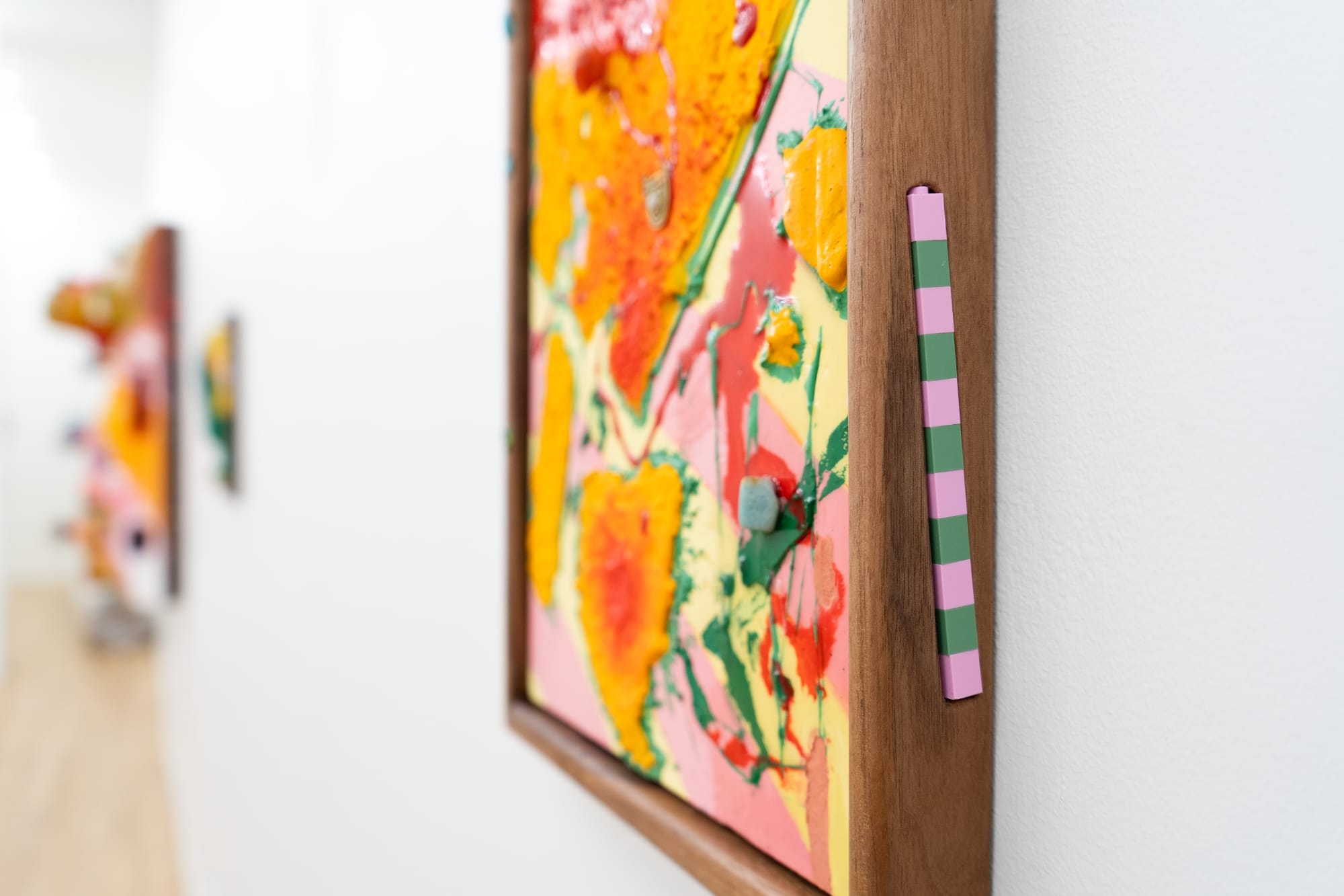 a side view of a green and pink striped object embedded in the wood frame of a colorful painting