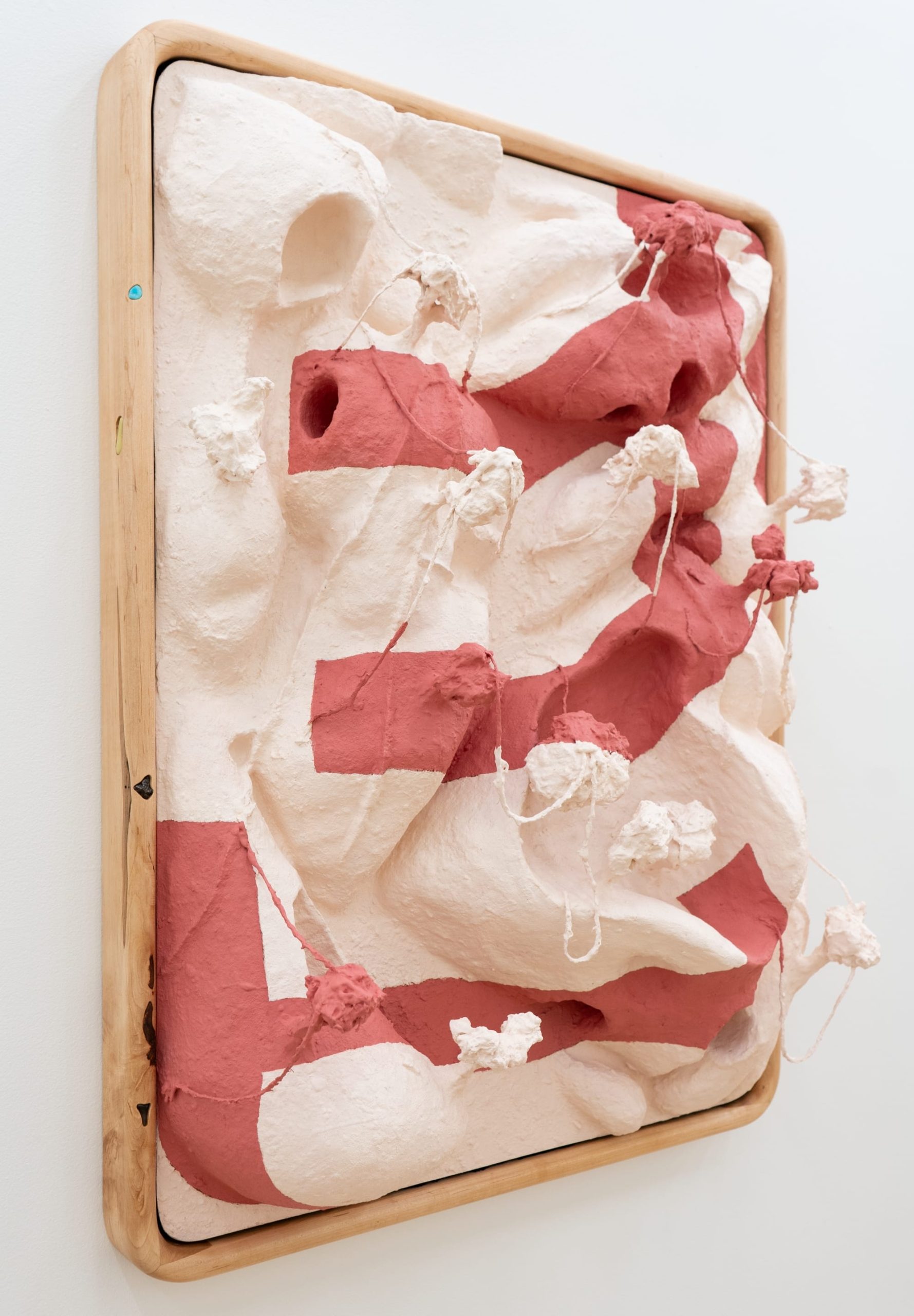a side view of a pink and white striped sculptural painting in a wood frame