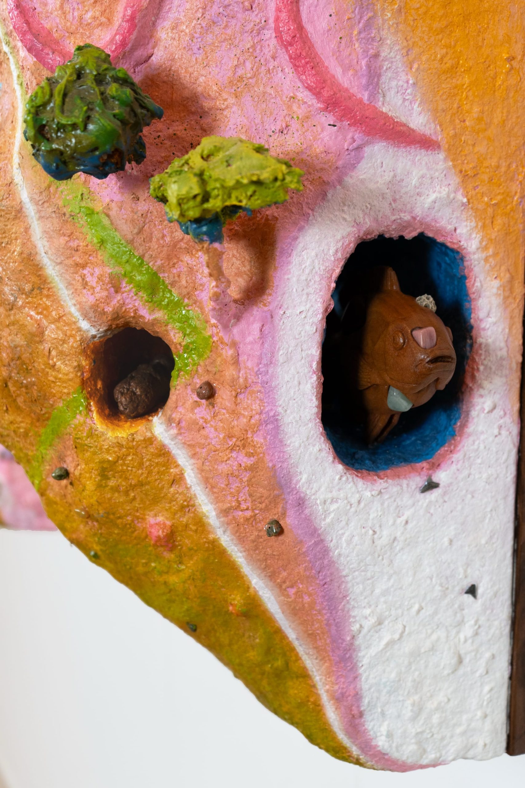 a carved wooden fish pokes out of a colorful sculptural painting