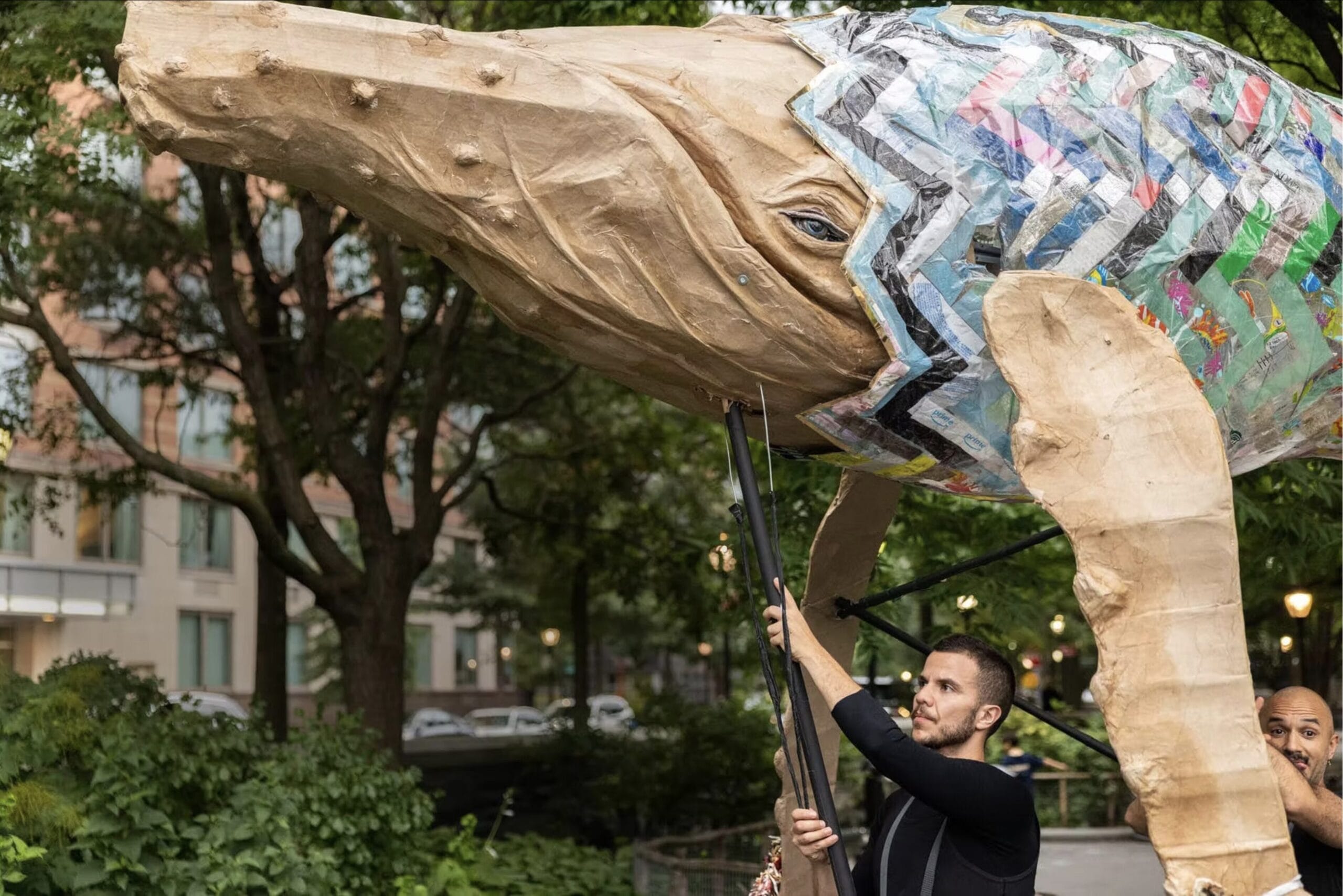 people carry a large puppet of a whale on a pole