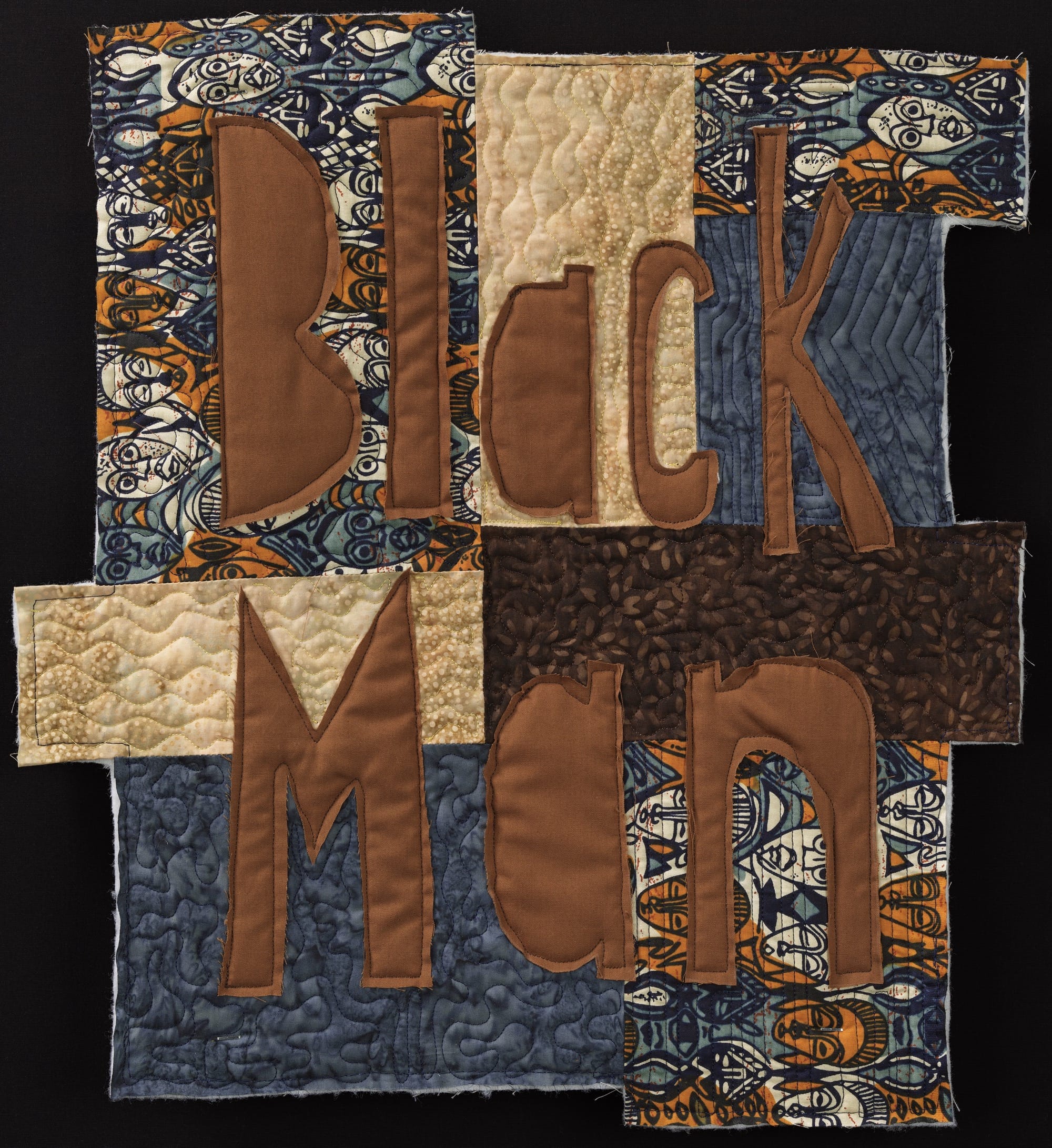 a small textile artwork with appliqued words "Black Man" in brown fabric