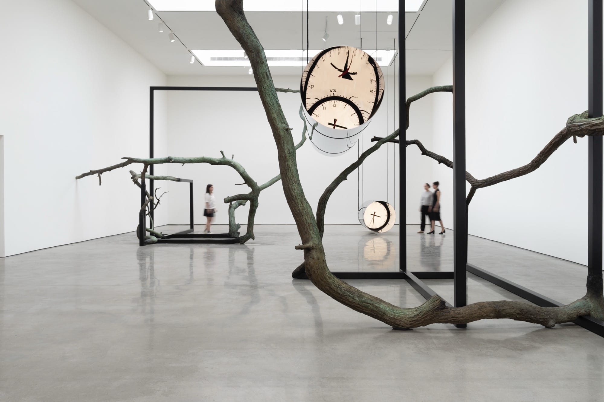 large suspended cylindrical metal sculptures with distorted clocks on the end suspend from a gnarled, tree like sculpture