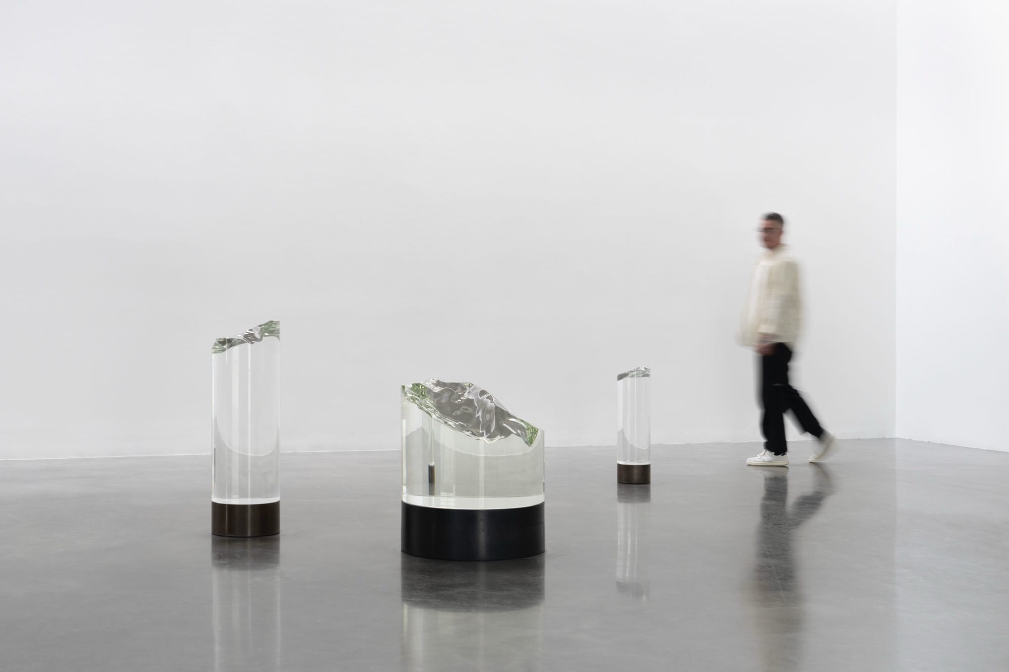 a person walks behind three glass sculptures in a gallery