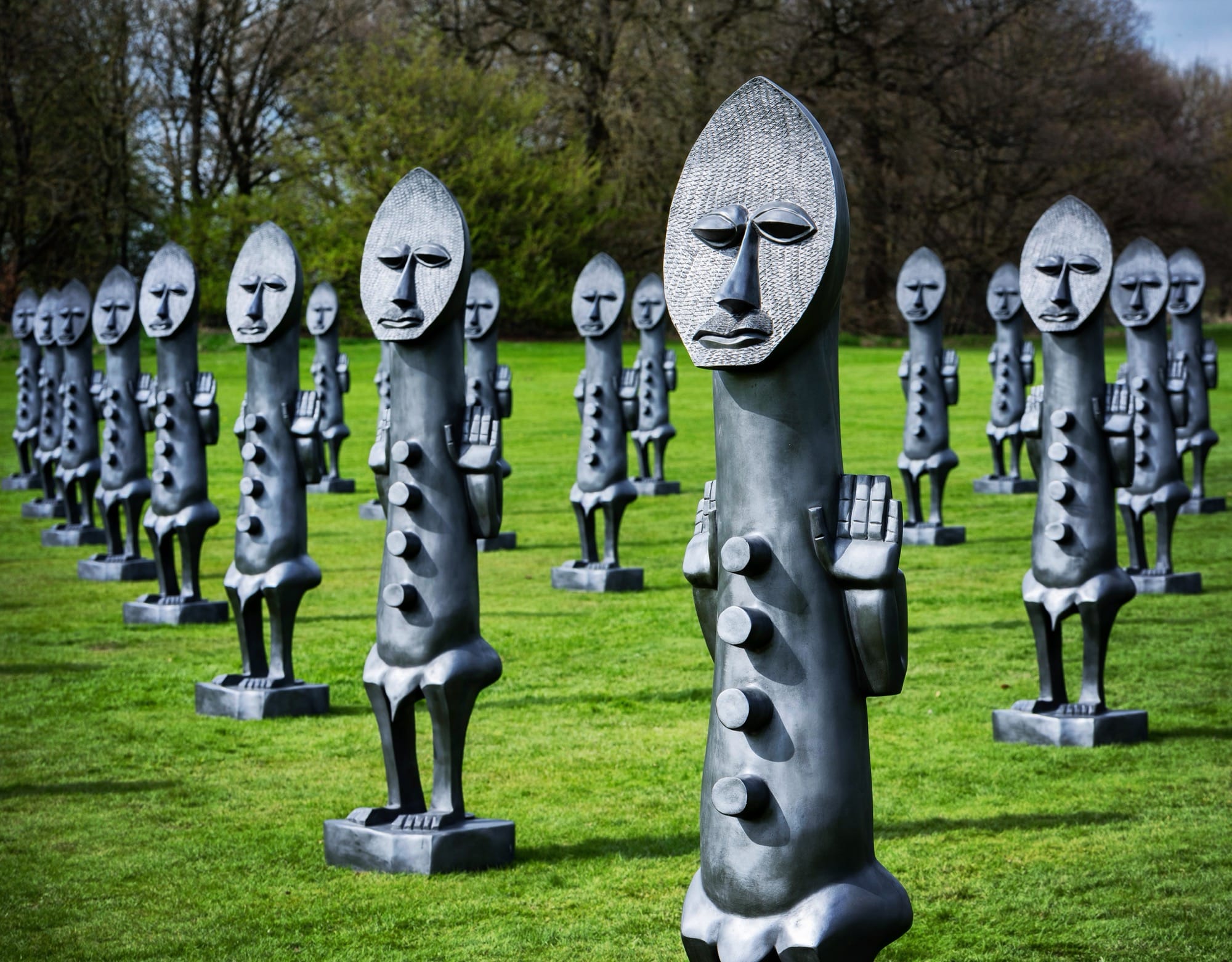 an installation on a lawn of numerous graphite figures resembling African sculptures