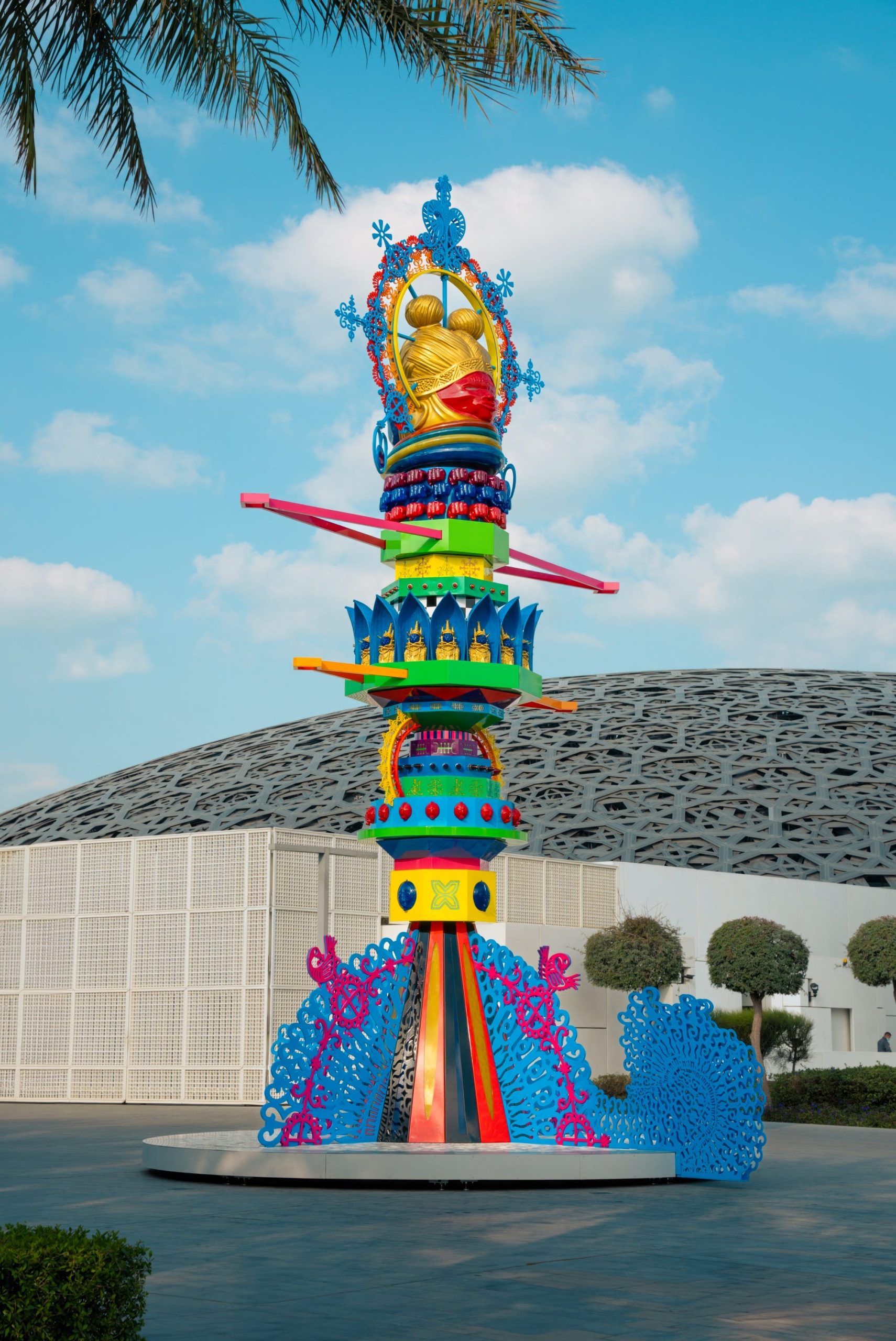 a vibrant, tall, totem-like sculpture outside of a contemporary museum building