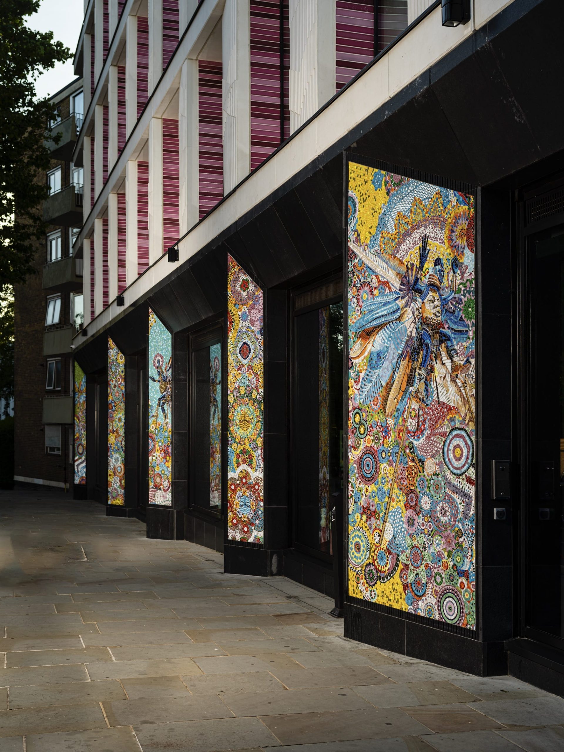 a series of vertical glass mosaic panels installed on the facade of a building in bright patterns and showing Black figures in colorful regalia