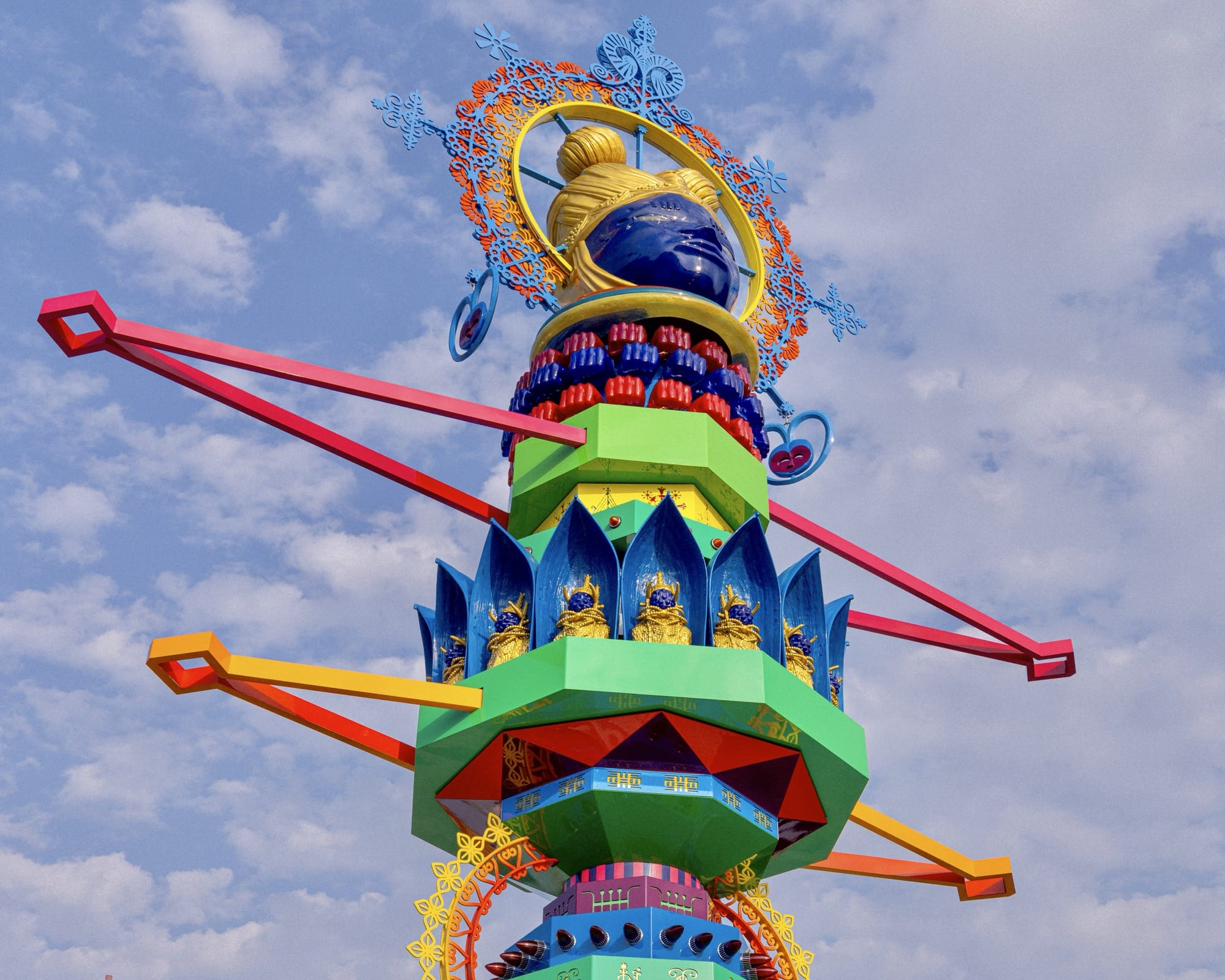 a detail of a vibrant, tall, totem-like sculpture with an African mask on the top and lace-like motifs