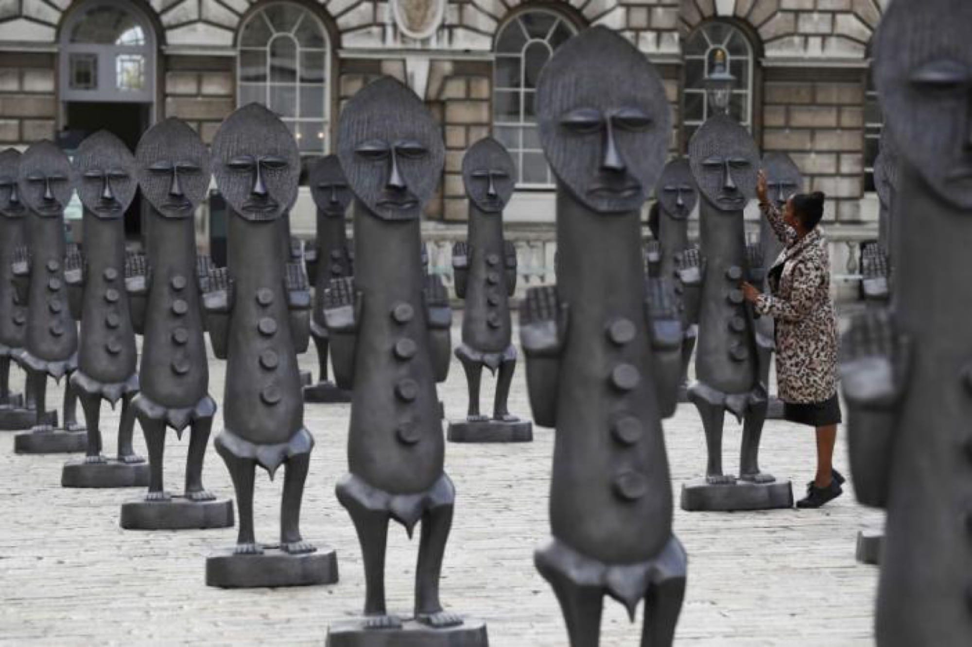 an installation in a courtyard of numerous graphite figures resembling African sculptures