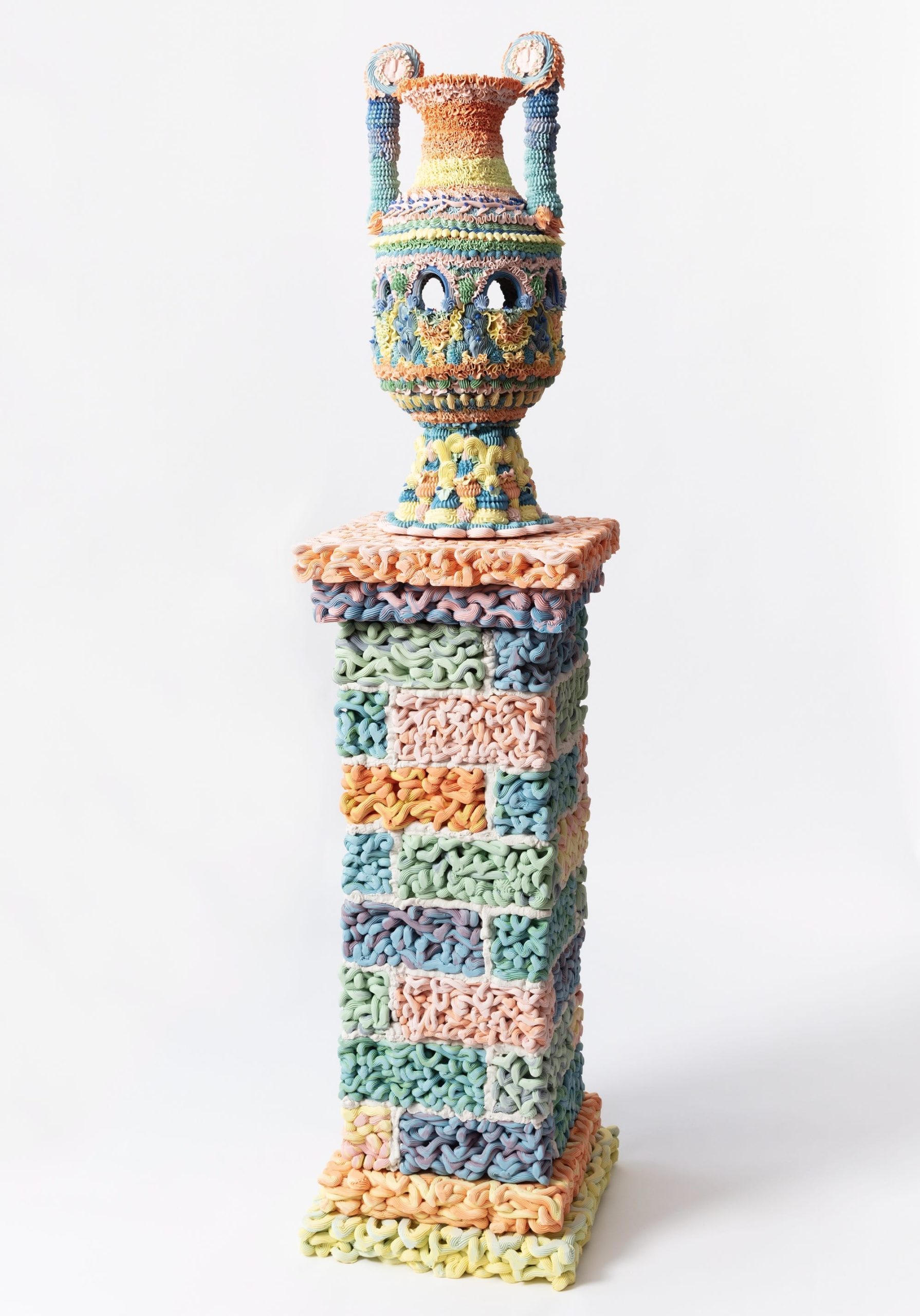 an elaborate, multi-colored ceramic vase on a decorated pedestal, made with clay piped like frosting