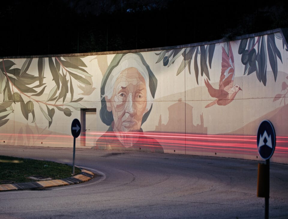 a mural of an elderly woman on a street barrier