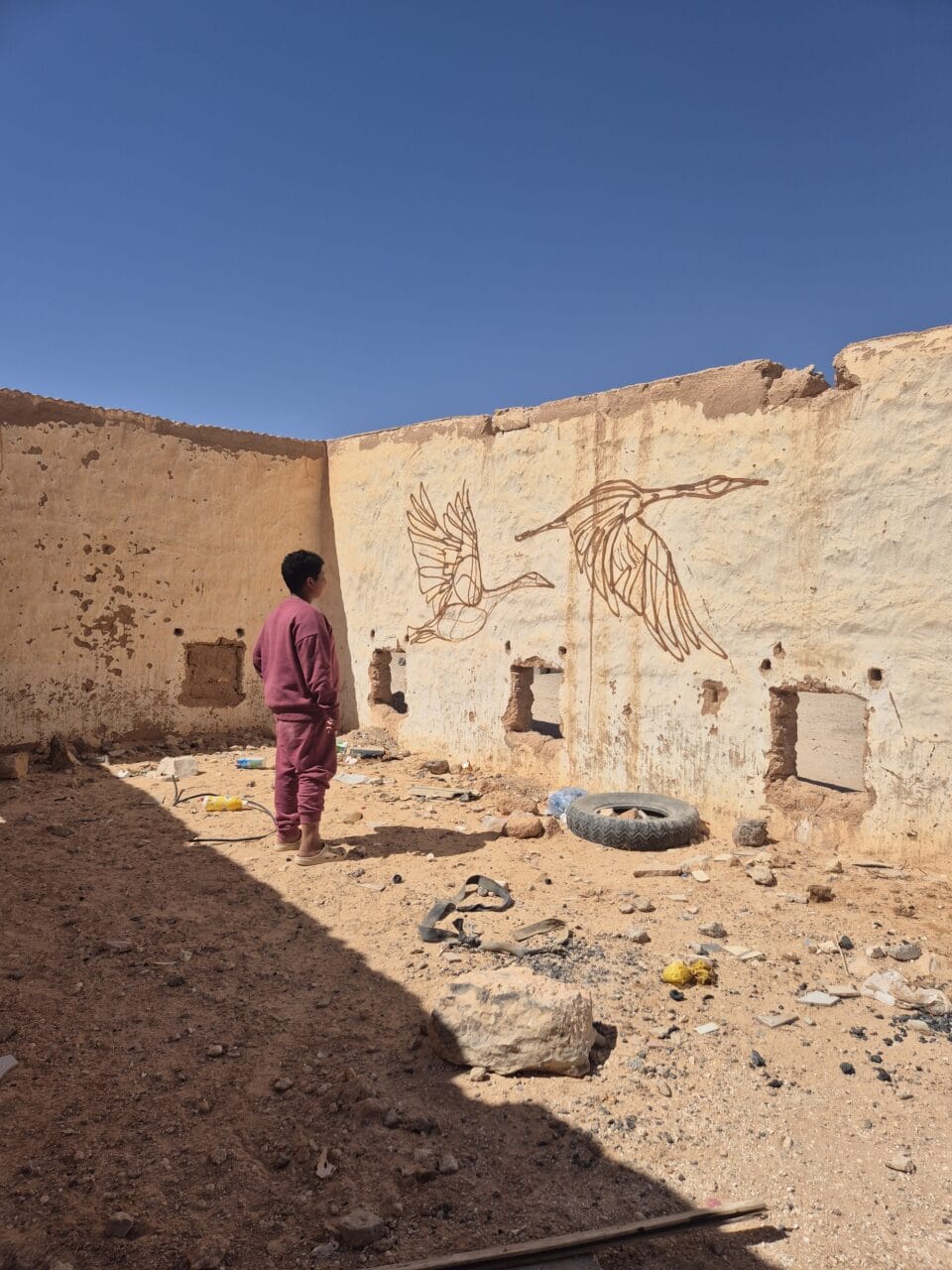 a mural of two birds flying on a stone wall. a small child stands before the work, admiring them